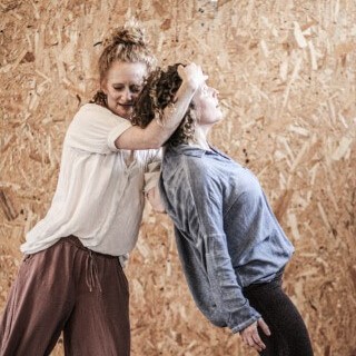 שתי נשים נעות אחת נשענת על השנייה עם הגב וההראשונה תומכת בה עם הגוף ועם היד על המצח